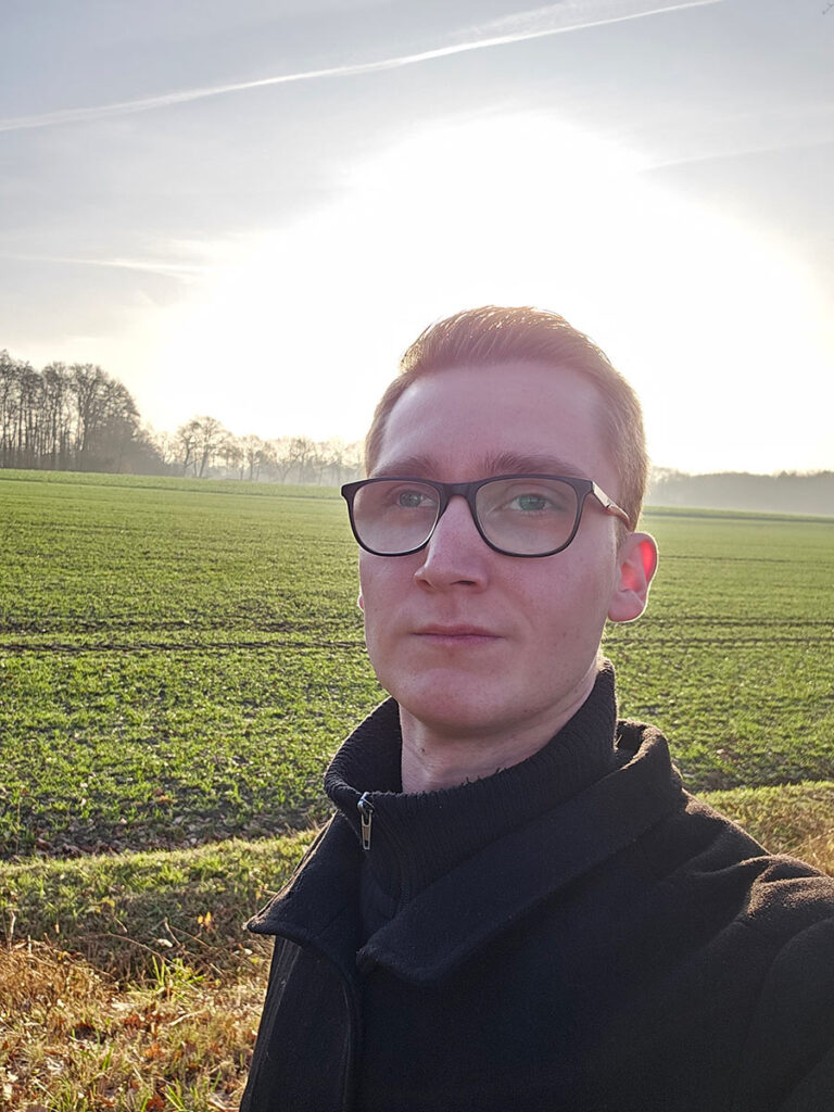 Portrait of Danny standing calmly in a field, illuminated by soft morning light during his custom tattoo calligraphy journey