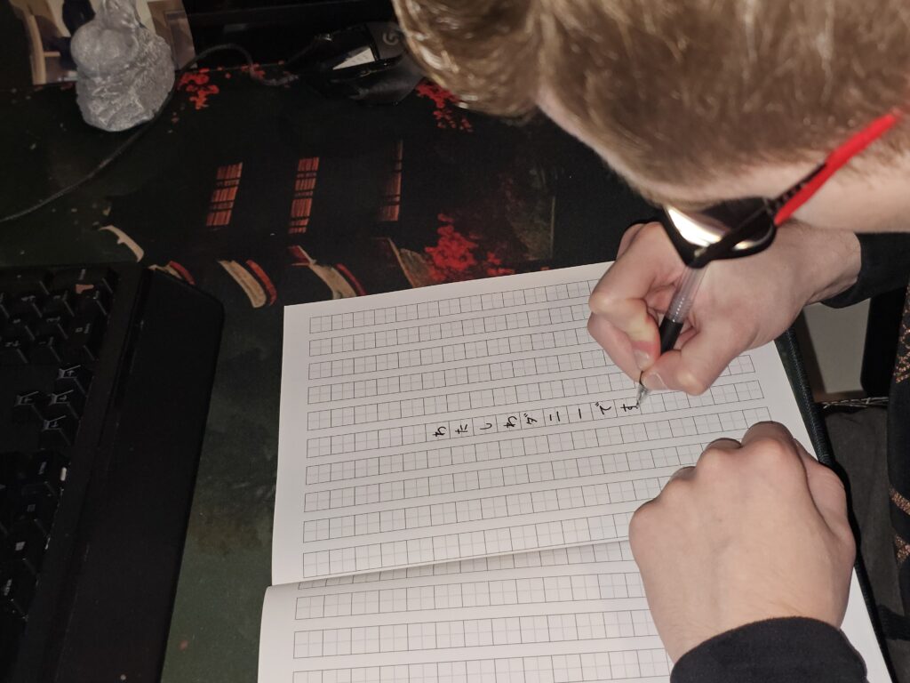 Danny carefully practicing Japanese characters in a notebook while preparing for a custom tattoo calligraphy design