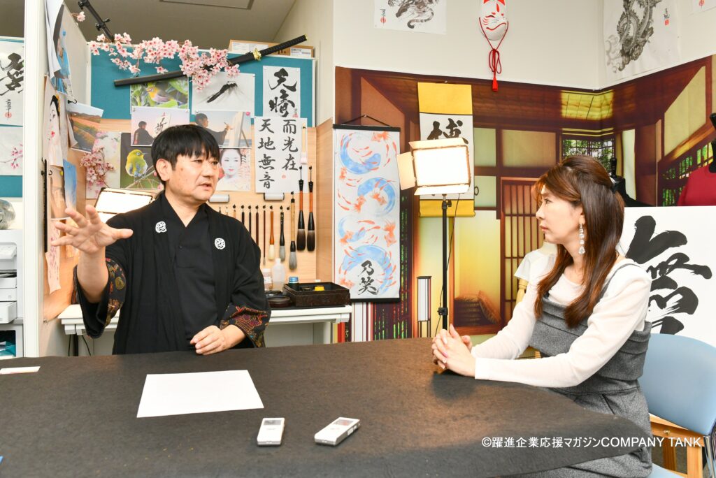Japanese calligraphy artist MADARA discussing the principles of Hisseki-jutsu during a COMPANY TANK magazine interview with TV personality Miho Yabe at the KANJI TOKYO studio.