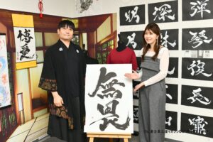 Japanese calligraphy artist MADARA standing with TV personality Miho Yabe during a COMPANY TANK magazine interview, showcasing a large Hisseki-jutsu calligraphy work at the KANJI TOKYO studio.