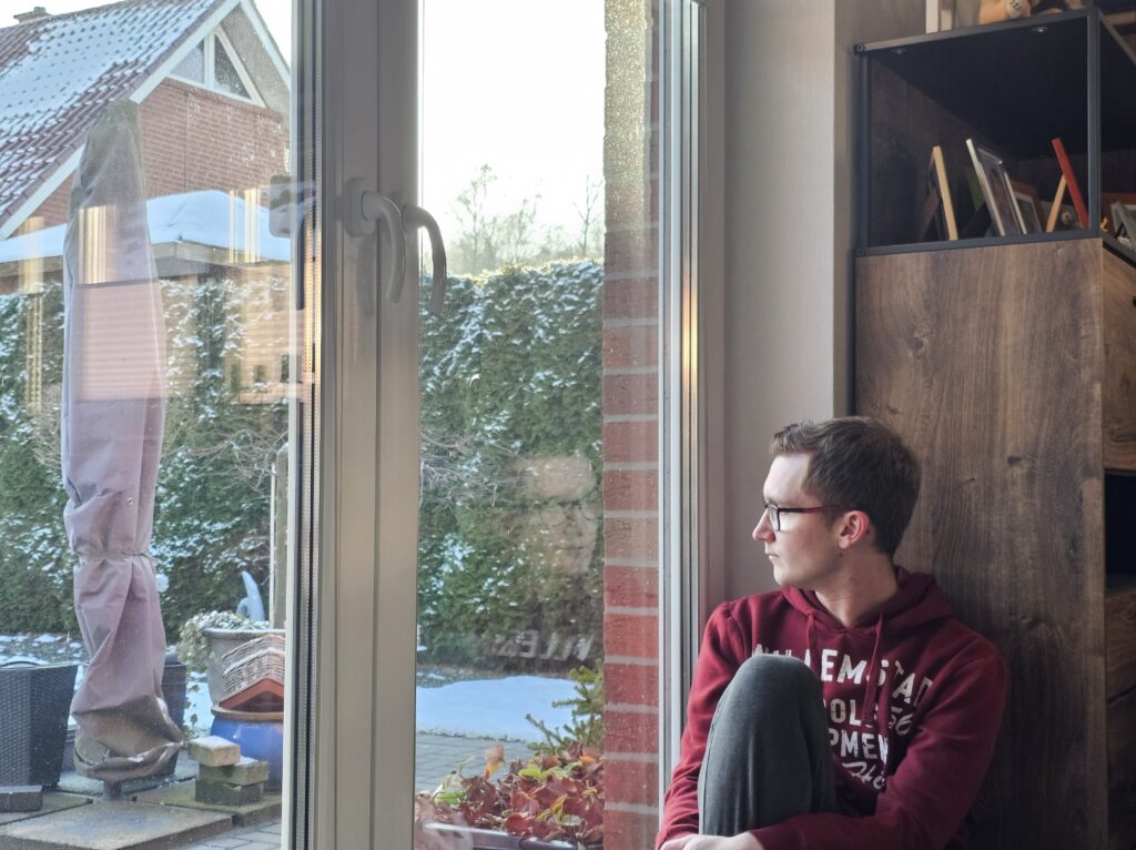 A man sitting by a window, quietly looking outside while reflecting on his inner thoughts