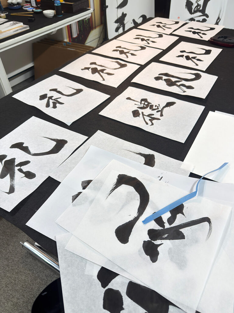 Calligraphy artist MADARA reviewing multiple brushstroke variations of the kanji “Rei” during the creation process for a custom kanji tattoo artwork