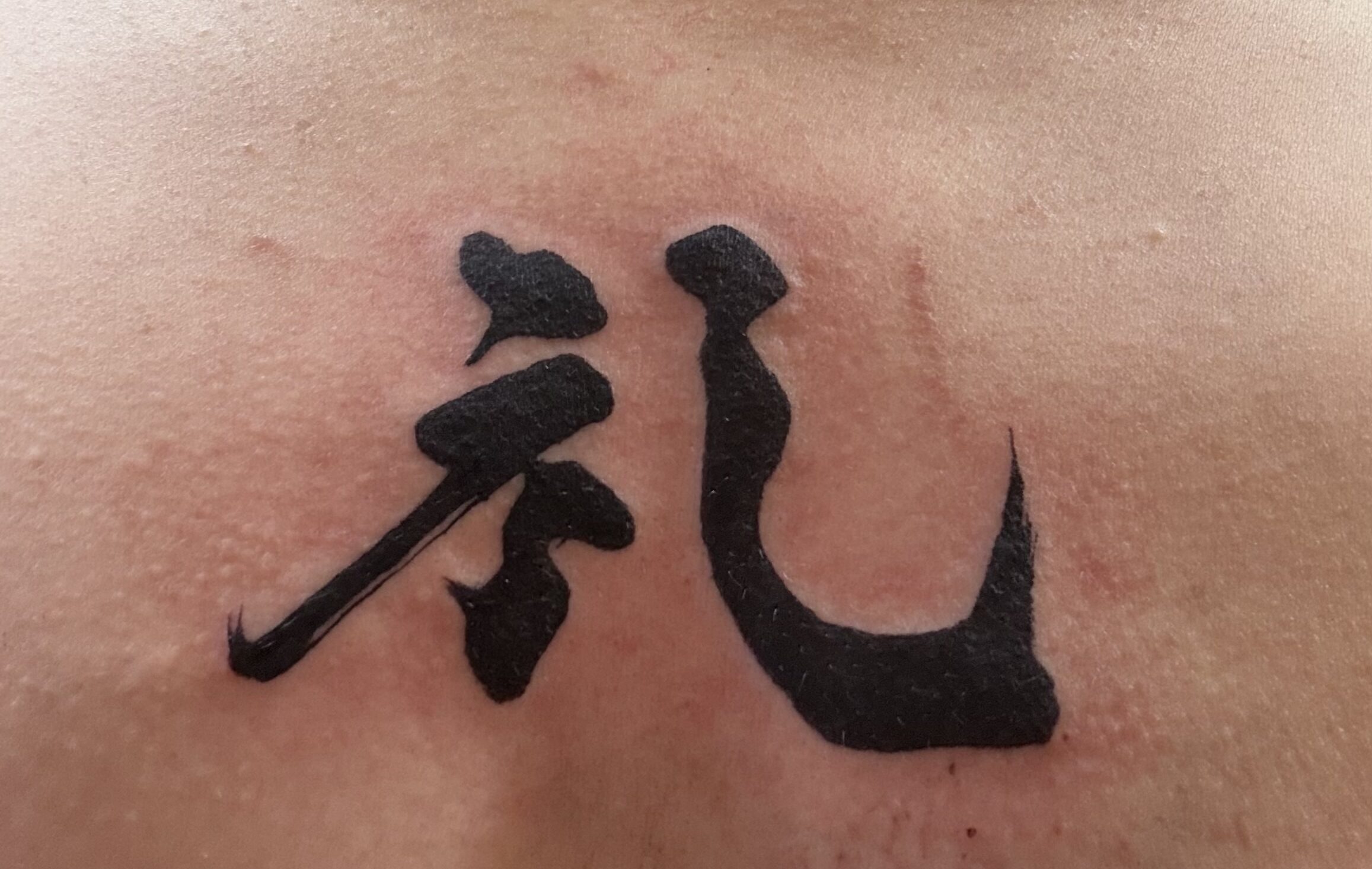 Kanji tattoo of “Rei” (礼) on the upper chest, created from Hisseki-jutsu calligraphy by calligraphy artist MADARA, symbolizing a personal vow and respect.