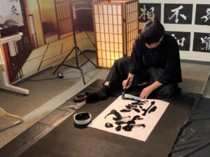 Calligraphy artist MADARA creating the kanji “Gaman” (endurance) for a custom tattoo design at KANJI TOKYO, carefully writing each stroke by hand during the production process.
