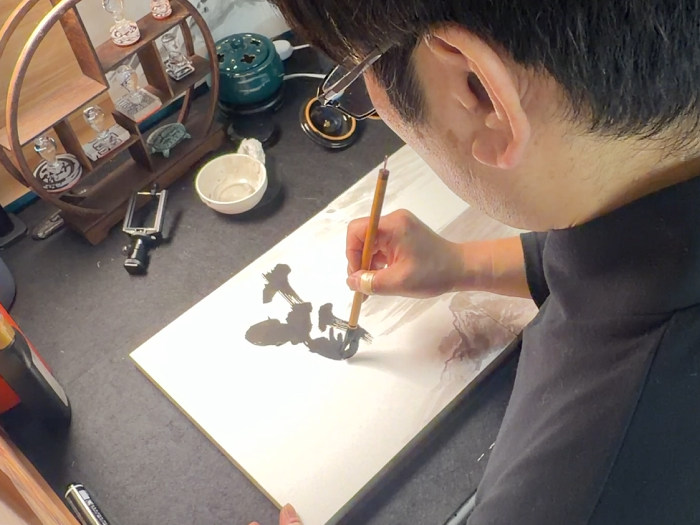 Madara practicing morning calligraphy as a warm-up before work, focusing quietly at his desk with brush and Sumi ink